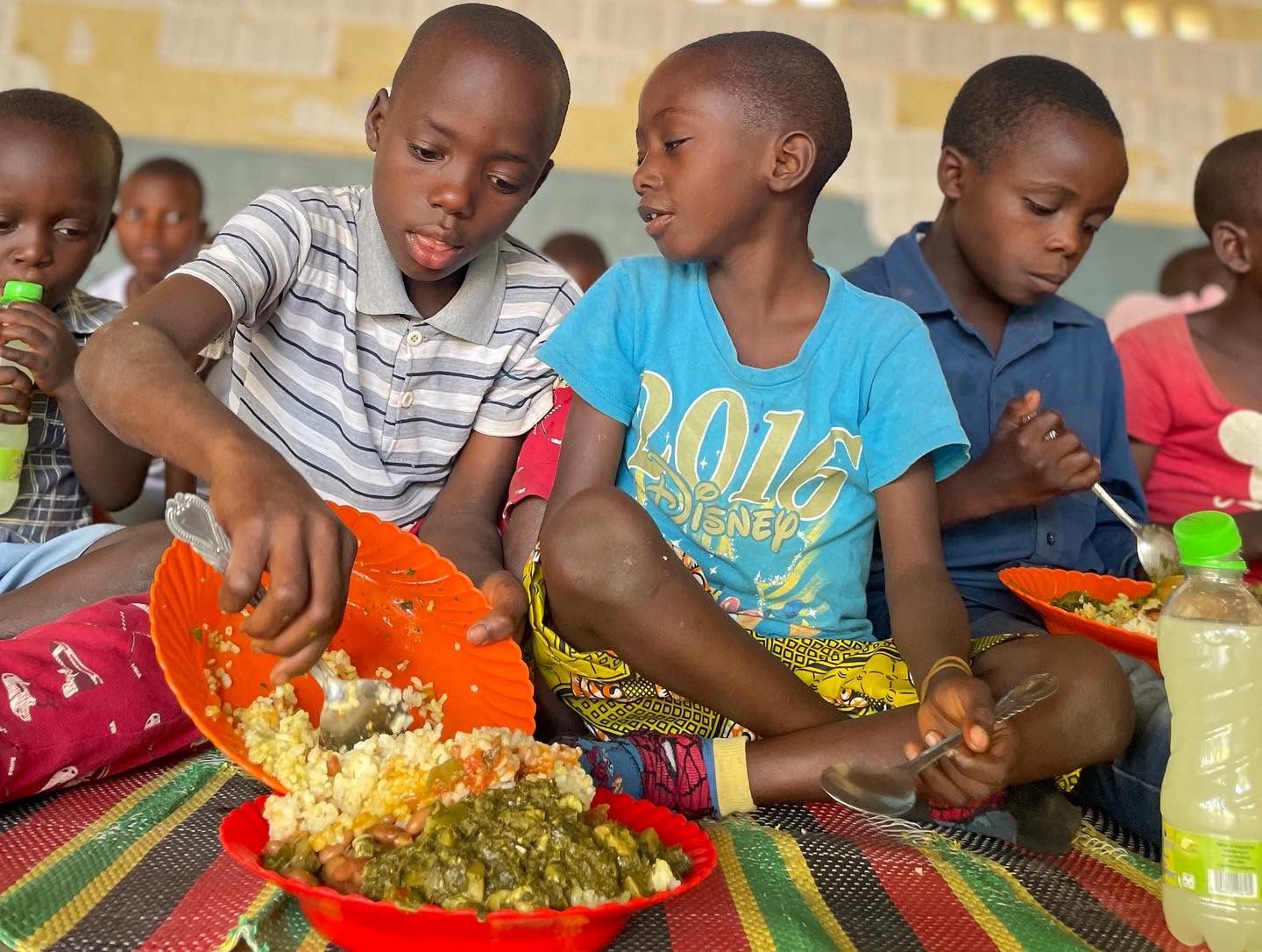 Children eating rice and vegetables from colorful bowls at a YBSP Sunday Meal