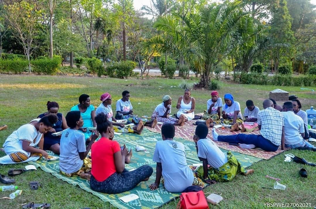 Women sitting in a circle on mats outdoors sharing a meal and discussion