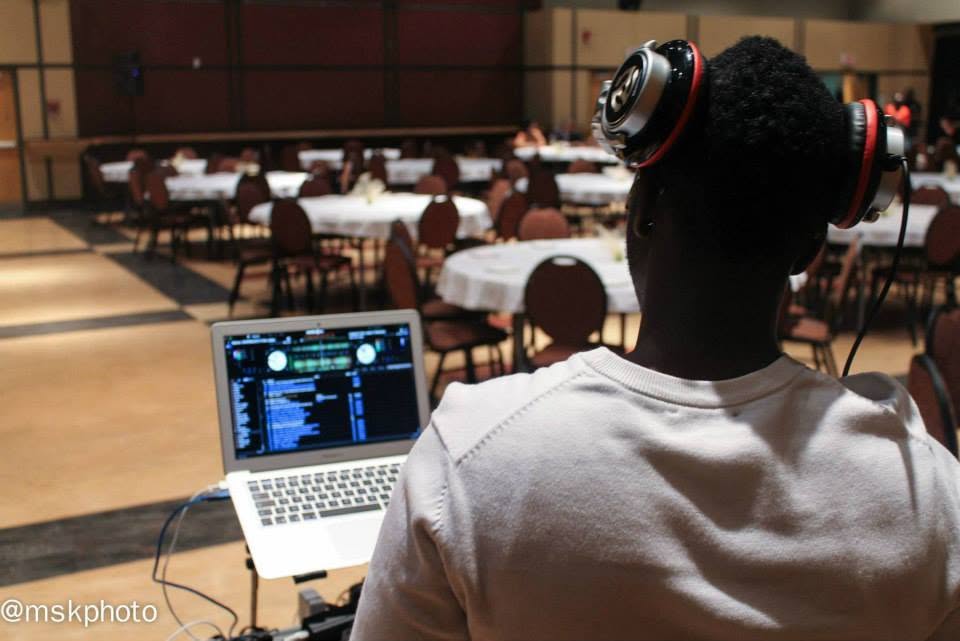 A DJ with headphones preparing music on a laptop in a decorated banquet hall