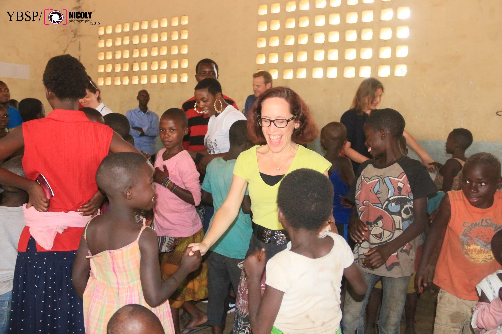 Volunteers and Burundian children laughing together during a joyful indoor group activity