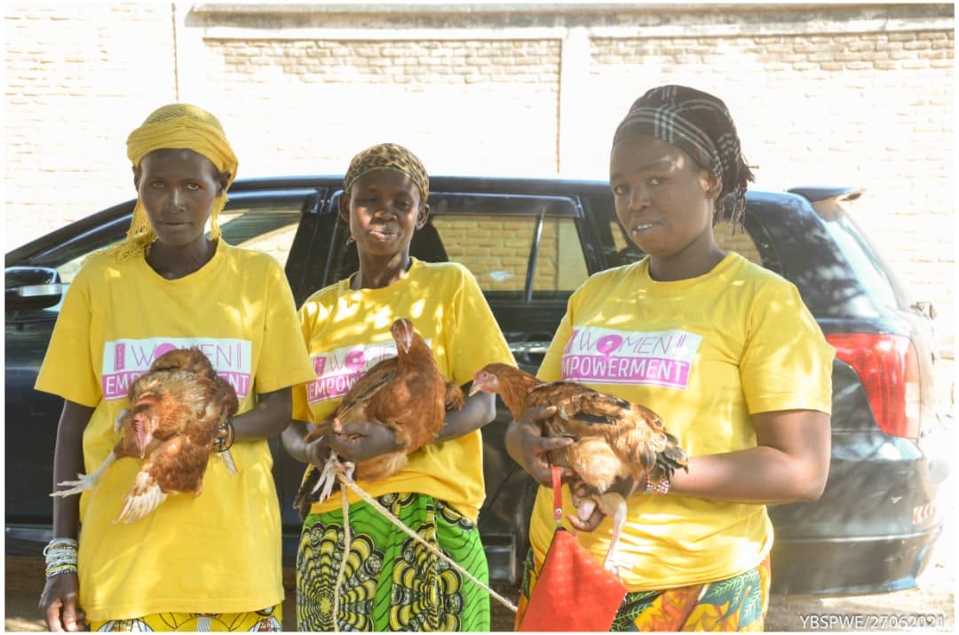Three women in Women Empowerment shirts holding chickens from a YBSP poultry livelihood project